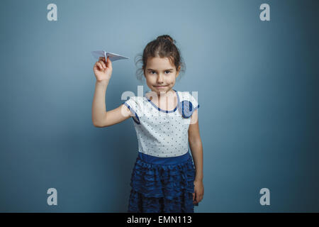 a girl of seven European appearance brunette holding a paper airplane on a gray background, smile Stock Photo