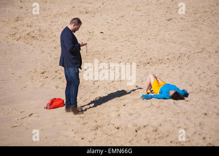 Bournemouth, Dorset, UK. 22nd April, 2015. Man stood using phone while woman lies on beach enjoying the sun at Bournemouth beach in April.  Credit:  Carolyn Jenkins/Alamy Live News Stock Photo