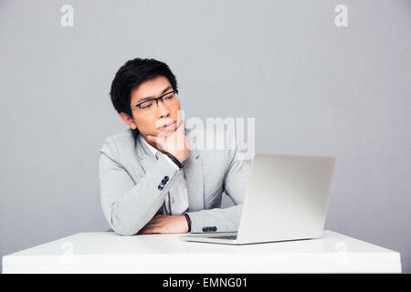 Thoughtful businessman sitting at the table with laptop over gray background Stock Photo