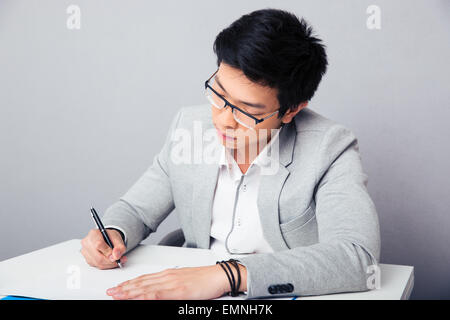 Young businessman sitting at the table and signing document over gray background Stock Photo