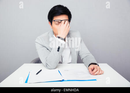 Tired businessman sitting at the table and rubs his nose in office Stock Photo