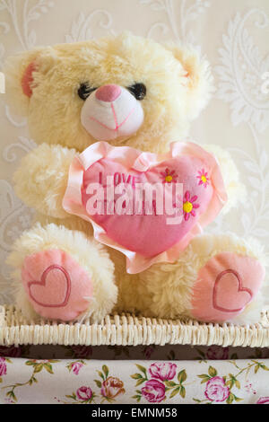 Teddy bear soft cuddly toy sat holding a pink heart with the words love to mum on it sitting on wicker basket - Mothers Day, Mothering Sunday gift Stock Photo