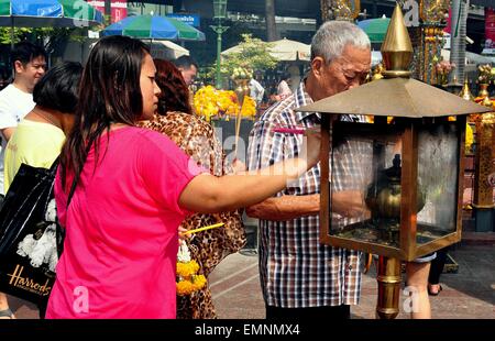 Bangkok, Thailand :  Elderly Thai man and a young woman lighting incense sticks from a flaming brass brazier Stock Photo