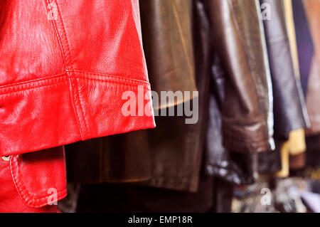 closeup of some used leather clothes, such as jackets and skirts, of different colors hanging on a rack in a flea market Stock Photo