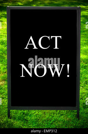 ACT NOW!  message on sidewalk blackboard sign against green grass background. Copy Space available. Concept image Stock Photo