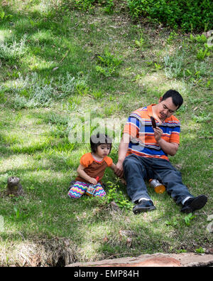 A Hispanic father takes pictures with his cell phone of his small daughter in a public park. Oklahoma, USA Stock Photo