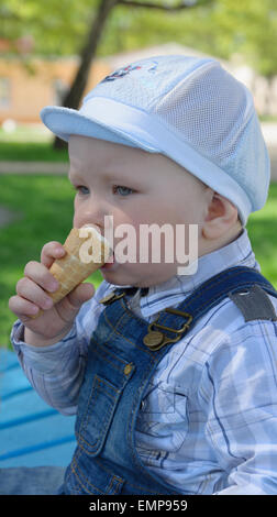 The boy in a jeans suit sits on a shop and eats ice cream. Stock Photo