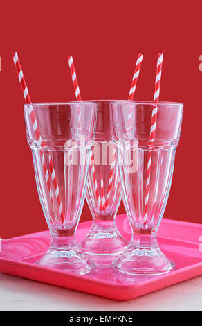 Empty soda pop glasses with straws on modern café style red and pink background on white vintage wood table. Stock Photo