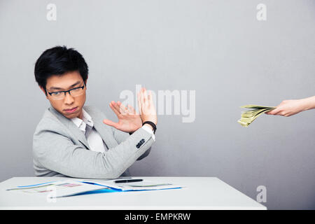 Asian young businessman gesturing stop sign while someone proposing money to him over gray background Stock Photo