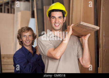 Carpenters Carrying Wooden Plank In Workshop Stock Photo