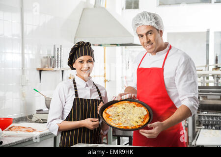 Happy Chefs Presenting Pizza At Commercial Kitchen Stock Photo