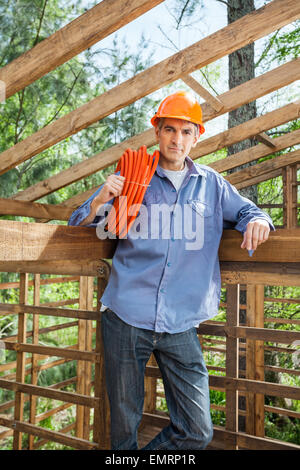 Confident Construction Worker Holding Pipe In Timber Cabin Stock Photo