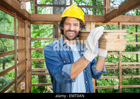 Happy Worker Carrying Wooden Planks On Shoulder Stock Photo