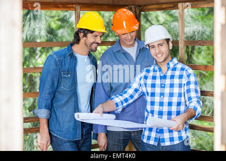 Happy Architect With Colleagues Analyzing Blueprint At Site Stock Photo