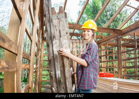 Female Worker Holding Ladder In Wooden Cabin At Construction Sit Stock Photo