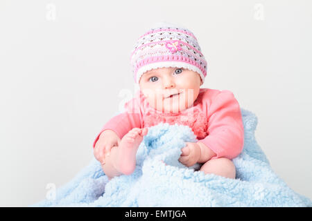 Little smiling baby girl sitting on blue blanket. She is wearing pink suit body and looking at camera Stock Photo