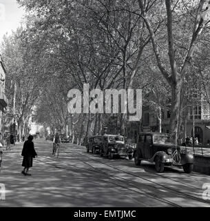 1950s, historical picture of a cyclist and cars parked in a tree lined avenue in the centre of Palma, Mallorca. Stock Photo