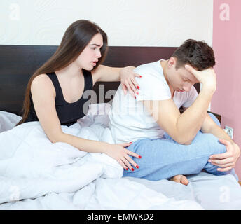 Depressed man sitting on edge of bed having problem against his woman. Young married couple who having problem in bed. Girl aspi Stock Photo