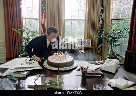 US President Ronald Reagan blows out candles on cake while celebrating his birthday party in the Oval Office of the White House February 5, 1982 in Washington, DC. Stock Photo