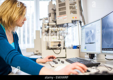 Pretty, female researcher using a microscope in a lab, doing research (color toned image) Stock Photo
