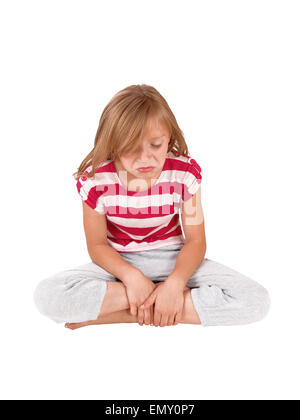 A little very unhappy girl sitting in her track pants and striped top on the floor and crying, isolated on white background. Stock Photo