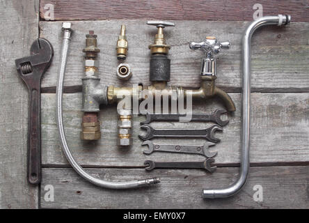 Plumber table components. Old rusty plumber pipes, crane, tubes, spanner set & water taps laying on dirty old wooden table. Stock Photo