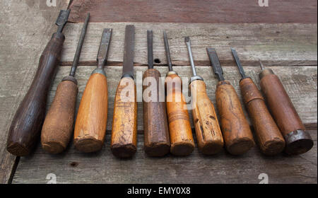 Carpenter tools row. Old carpenter chisels, screw driver, file & awl laying on dirty wooden table angle view. Stock Photo