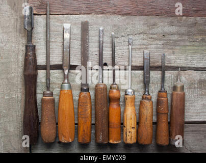 Carpenter tools composition. Old carpenter chisels, screw driver, file & awl laying on dirty wooden table upper view. Stock Photo