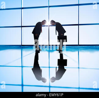 Two businessmen Bowing in Back Lit Stock Photo