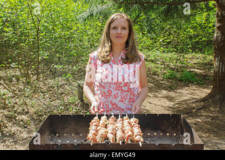 The young girl in a blouse fries a shish kebab on skewers in a brazier. Stock Photo