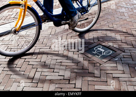 A bike sign on the road with the shadow of a cyclist going by Stock Photo