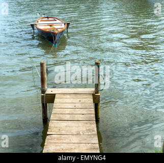 A small rowing boat moored to a wooden jetty on the banks of the Tresillian river in Cornwall Stock Photo