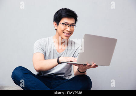 Smiling asian man using laptop over gray background Stock Photo