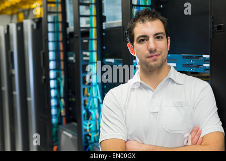 A happy data center manager posing in front of the data center equipment racks Stock Photo
