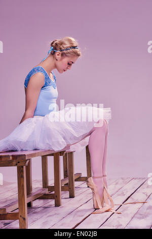 Tired ballet dancer sitting on the wooden floor Stock Photo
