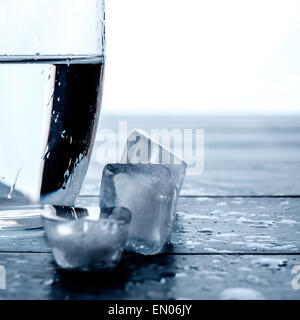 Glass of water and melting ice cubes on a wooden table Stock Photo