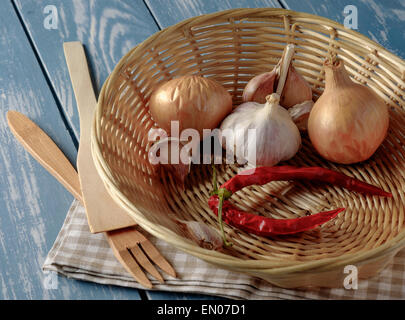 Basket with onions, garlic and red pepper on a wooden table. Stock Photo