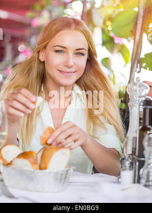 Portrait of beautiful blond woman sitting at outdoors cafe and eating bread, waiting for someone, spending summer vacation Stock Photo