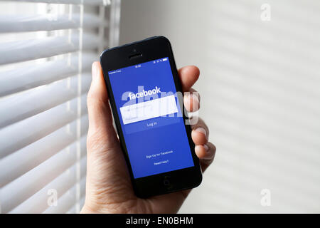 Hand holding Iphone with mobile application for Facebook on the screen Stock Photo