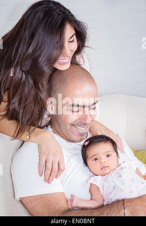 Happy parents with adorable little baby girl sitting on the couch at home, enjoying parenthood, young happy family, new life con Stock Photo