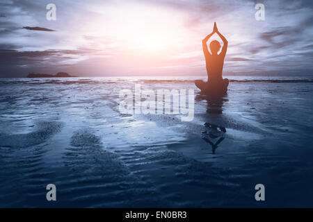 well being concept, beautiful sunset on the beach, woman practicing yoga Stock Photo