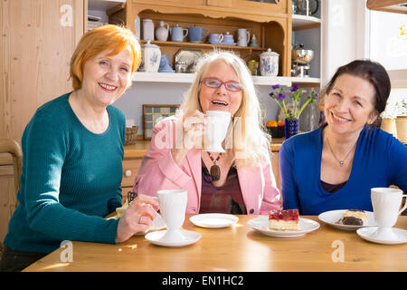 Three Smiling Mom Friends Sitting at the Wooden Table with Tasty Snacks and Looking at Camera. Stock Photo