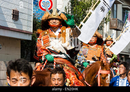 Japanese man dressed in full samurai armour on horseback smiling at viewer while riding through city street in the Genji parade at Tada in Japan. Stock Photo