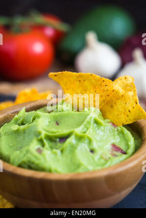 Guacamole in Wooden Bowl with Tortilla Chips and Ingredients Close Up Stock Photo