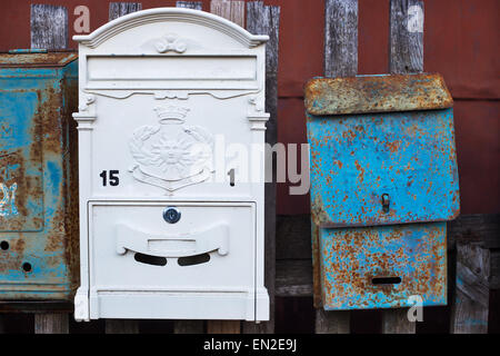 Two different mailboxes: new white and old with rust attached to the fence Stock Photo