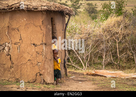 Two small Masai children peek out from a mud hut in a Masai Village. The huts form a kraal and is fenced by acacia thorn bushes. Stock Photo