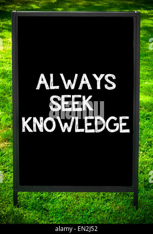 ALWAYS SEEK KNOWLEDGE  message on sidewalk blackboard sign against green grass background. Copy Space available. Concept image Stock Photo