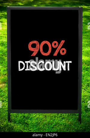 NINETY PERCENT DISCOUNT  message on sidewalk blackboard sign against green grass background. Copy Space available. Concept image Stock Photo