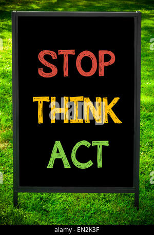 STOP, THINK, ACT  message on sidewalk blackboard sign against green grass background. Copy Space available. Concept image Stock Photo