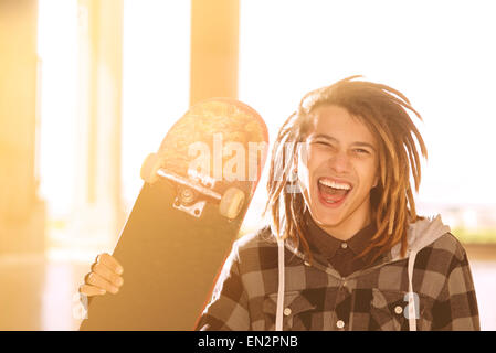portrait of young guy  with skateboard and rasta hair in a lifestyle concept warm filter applied Stock Photo
